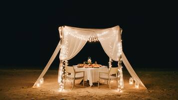 A tented dining area with a table set for two, surrounded by string lights and candles.