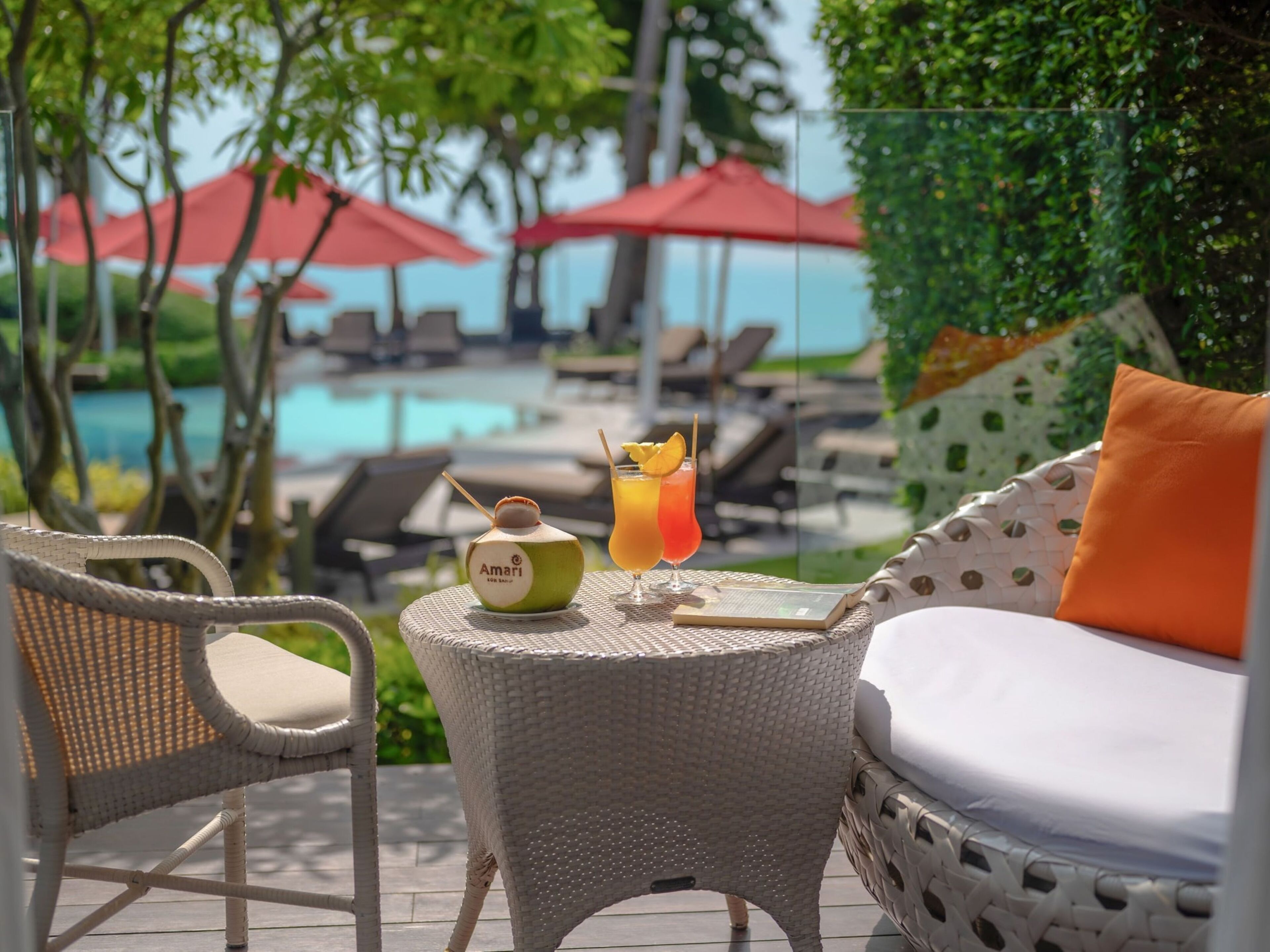 A wicker lounge chair with a cushion and a small table with a drink and a coconut.