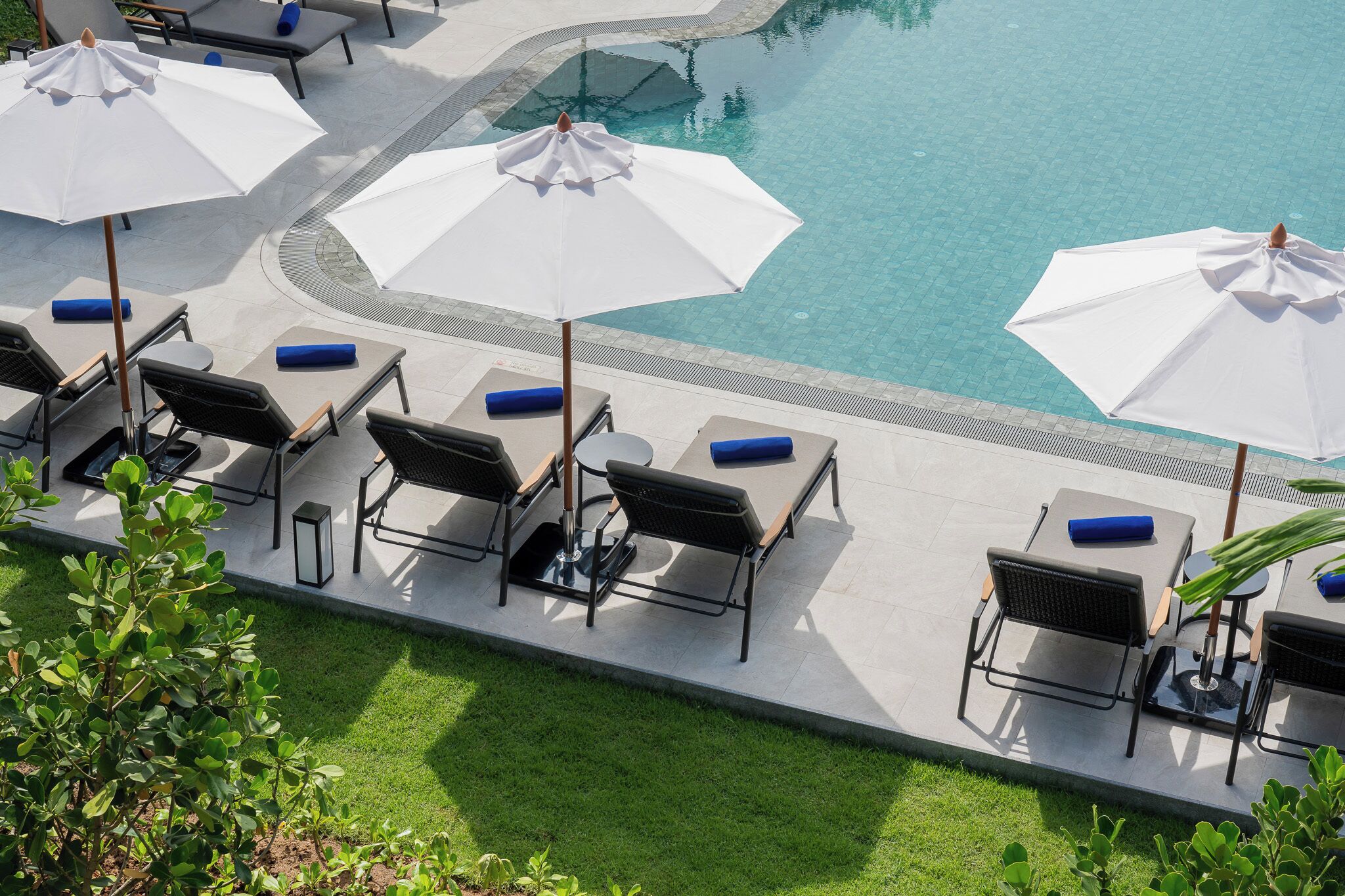 A poolside area with multiple white umbrellas, lounge chairs, and a clear view of the pool.