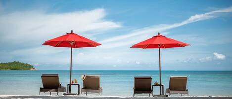 Two beach chairs under red umbrellas with a view of the ocean and a distant island.