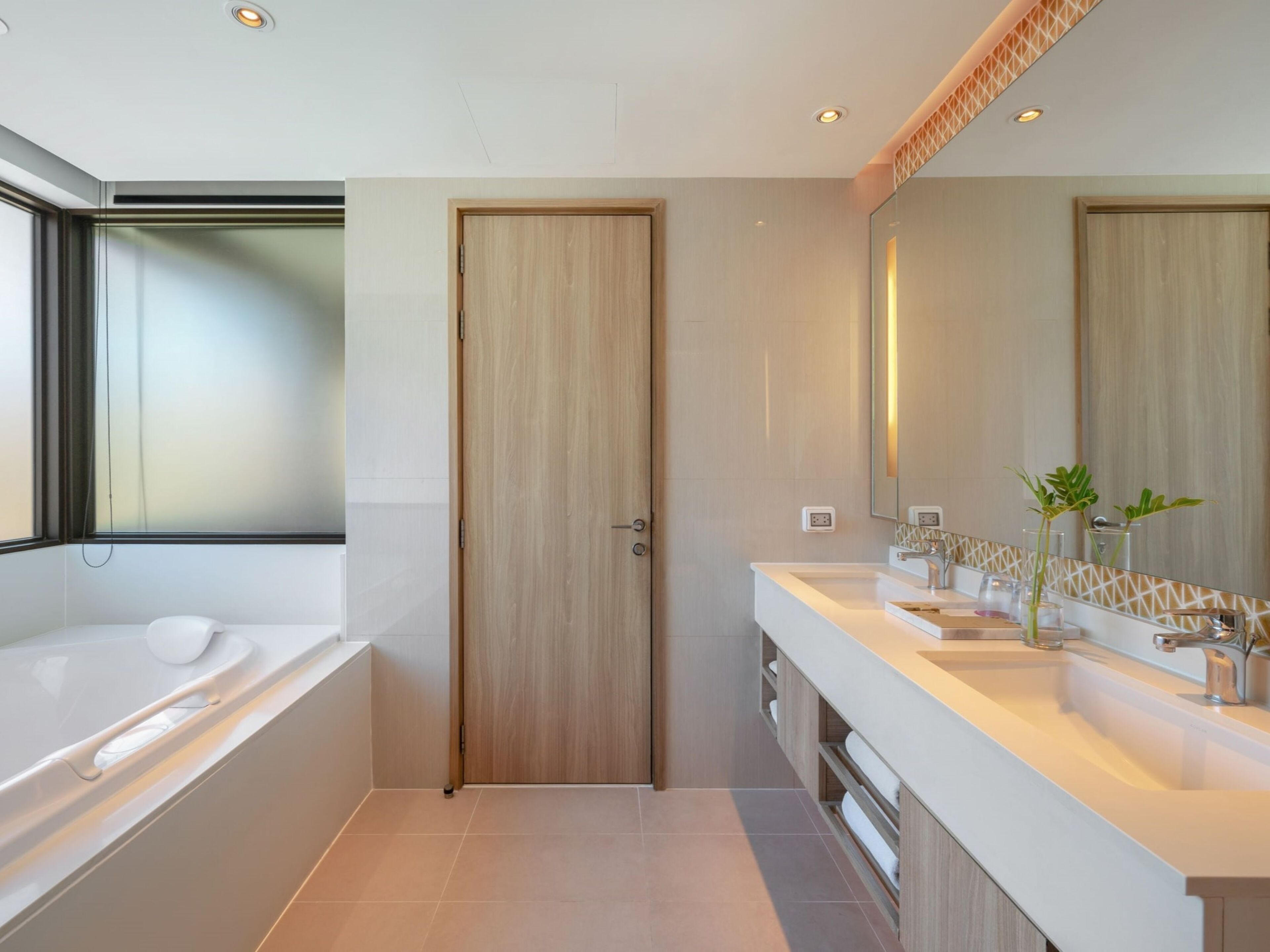 A modern bathroom with a wooden door, a large mirror, and a dual sink vanity.