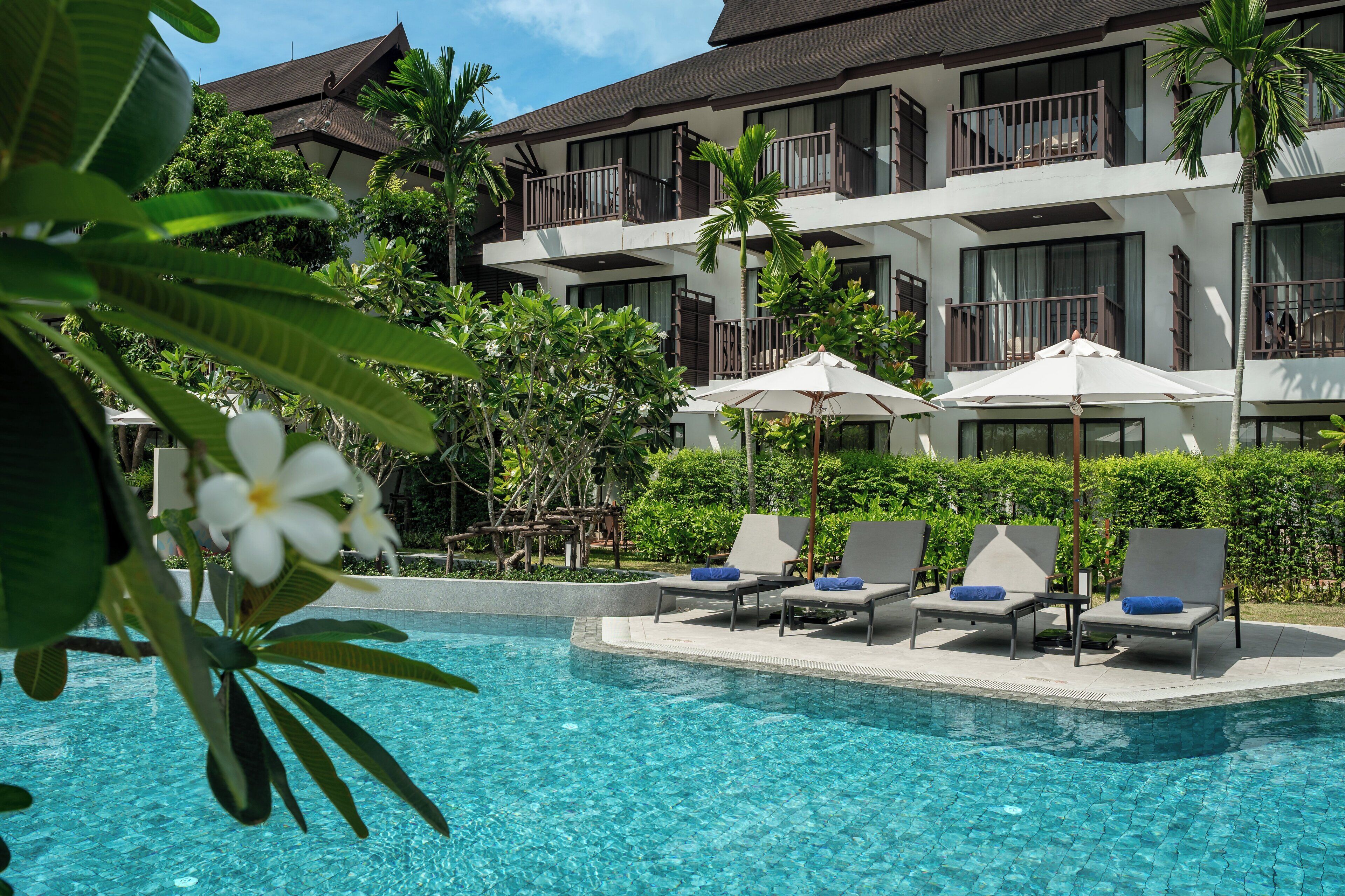 A hotel with a pool area, lounge chairs, and umbrellas.