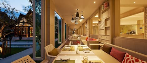 A dining area with a long table set for a meal, surrounded by seating with cushions.