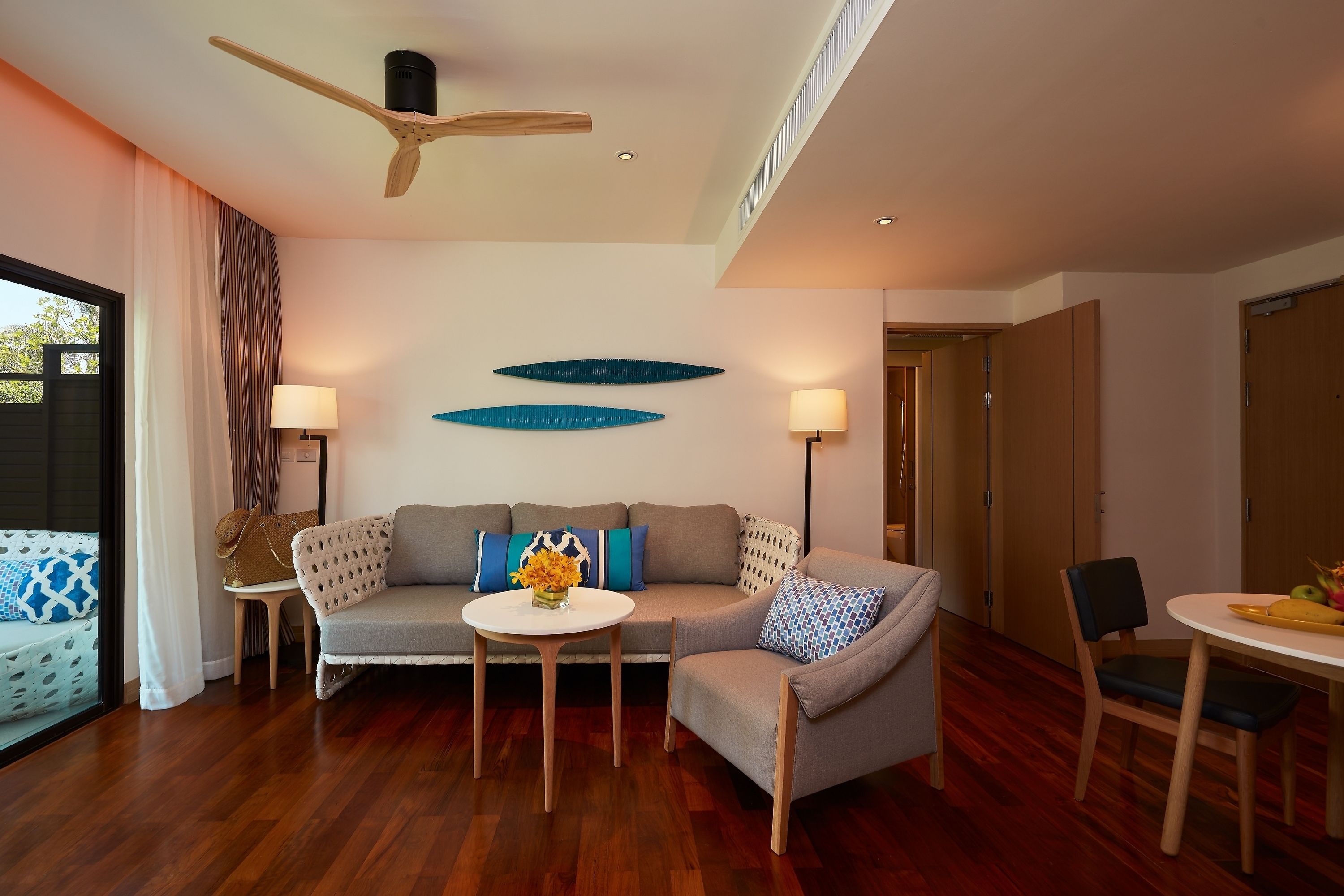 A modern living room with a sofa, two side tables, a dining table, and a ceiling fan.