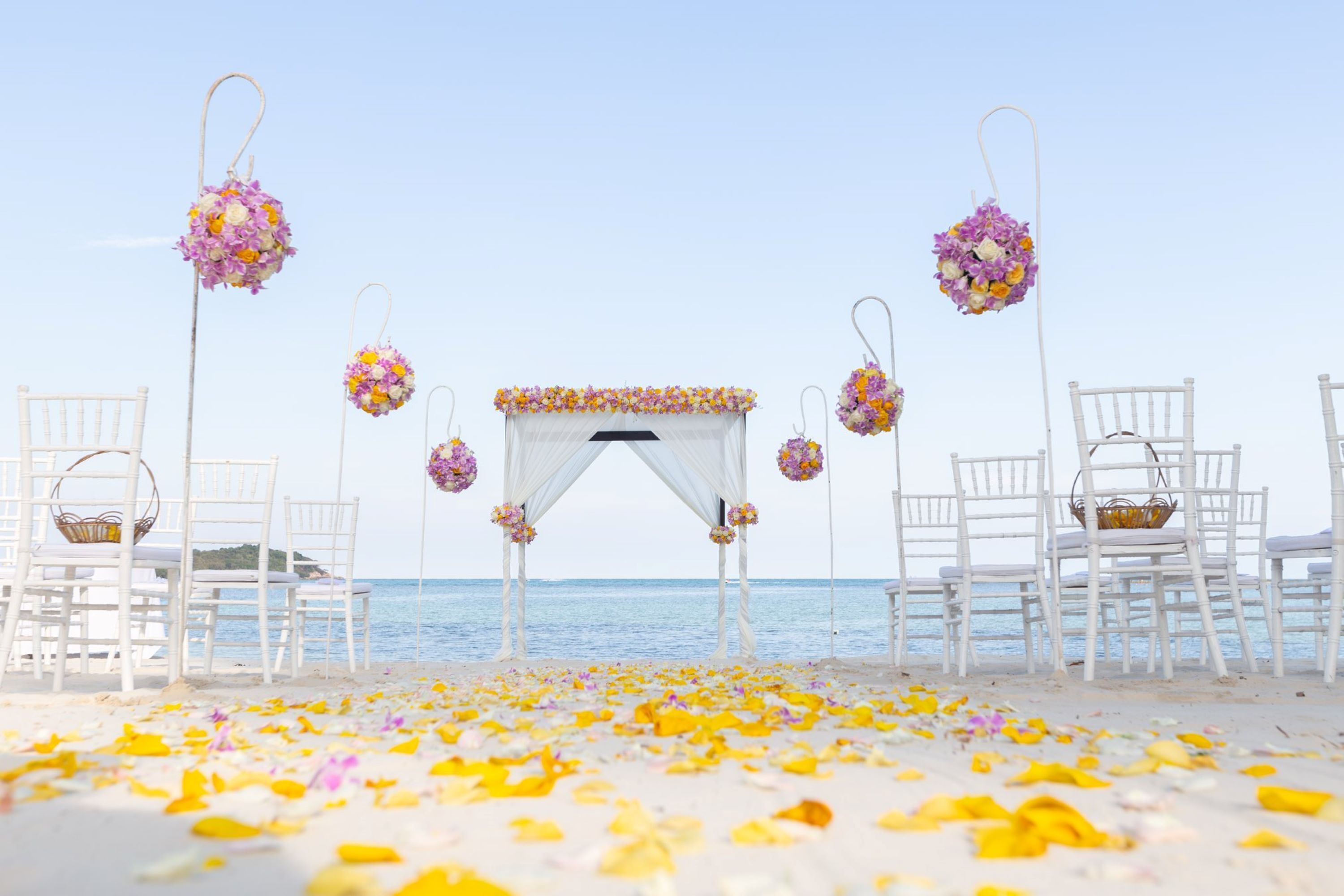 A beach wedding setup with white chairs and a floral arch.