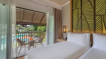 A hotel room with a large bed, a balcony with a view of a pool and greenery, and a decorative wall panel.