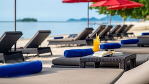 Un espace de détente aménagé au bord de la plage, avec des chaises longues, des parasols rouges et une vue dégagée sur la mer.