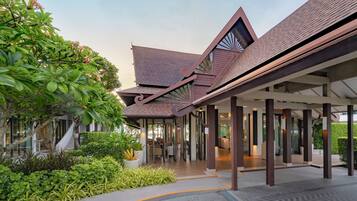 A modern building with a covered walkway, surrounded by lush greenery and a clear sky.