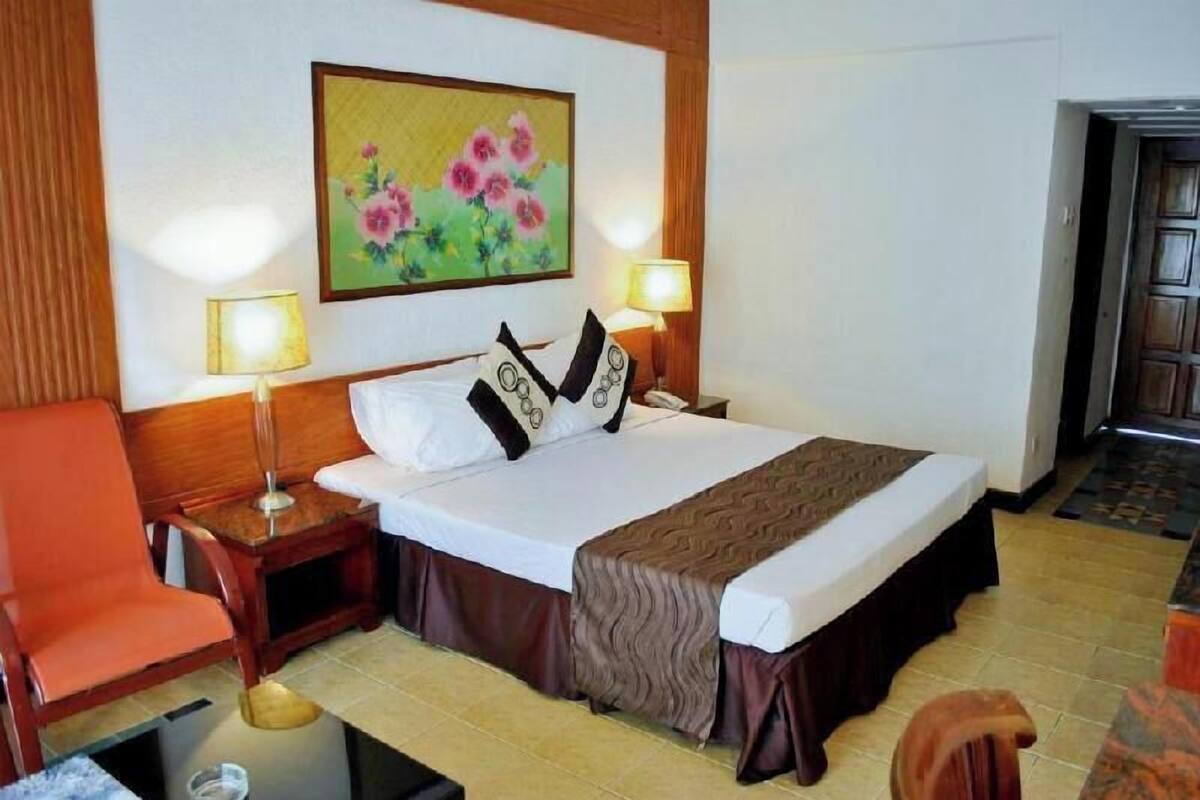 A hotel room with a bed, two bedside lamps, a painting, a chair, and a small table.