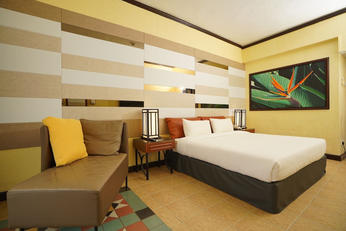 A hotel room with a bed, a sofa, a nightstand, and a wall-mounted lamp.