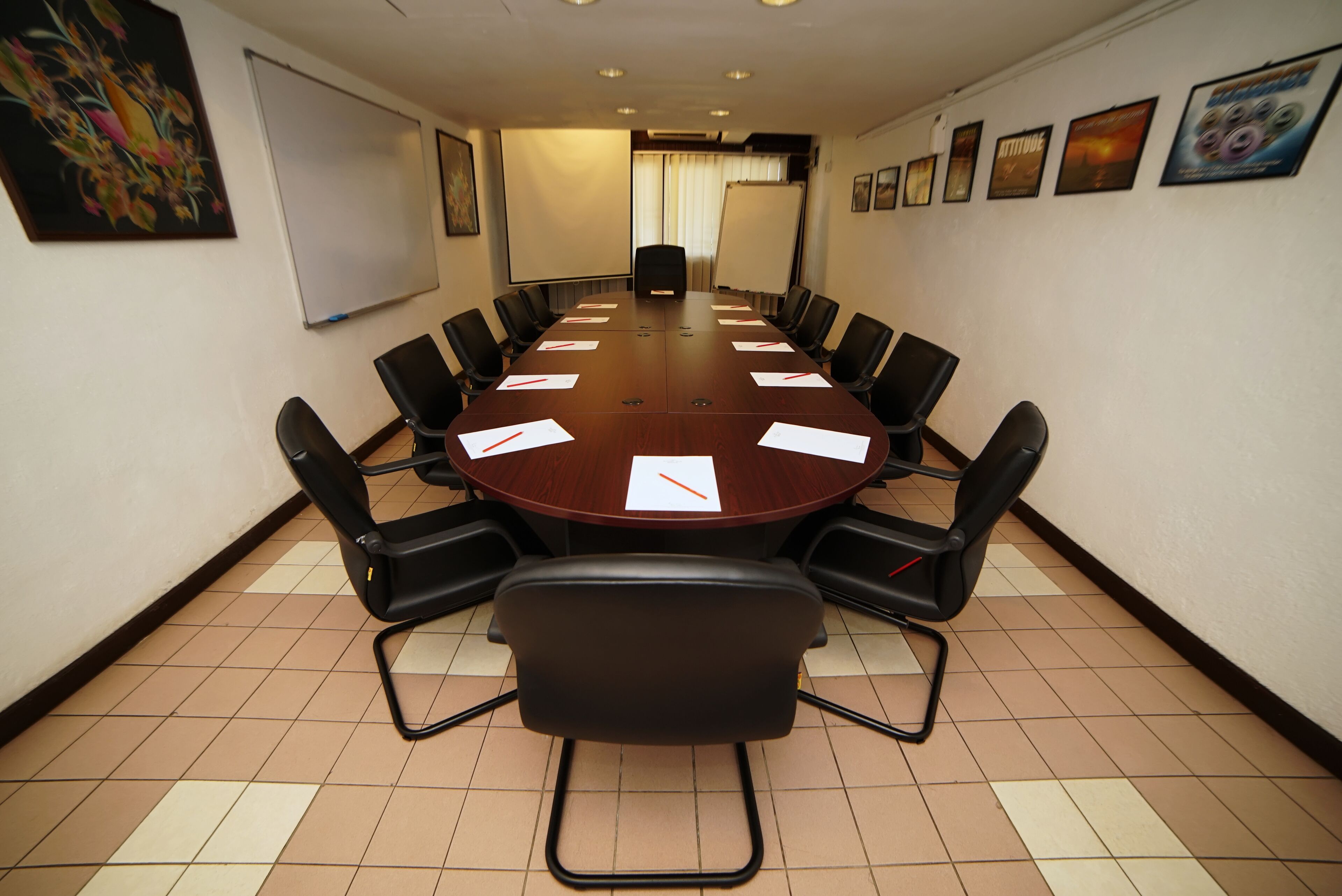 A conference room with a large oval table, black chairs, a whiteboard, and a projector screen.