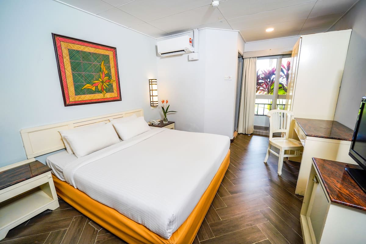 A hotel room with a bed, bedside table, air conditioning unit, and a view of the outside.