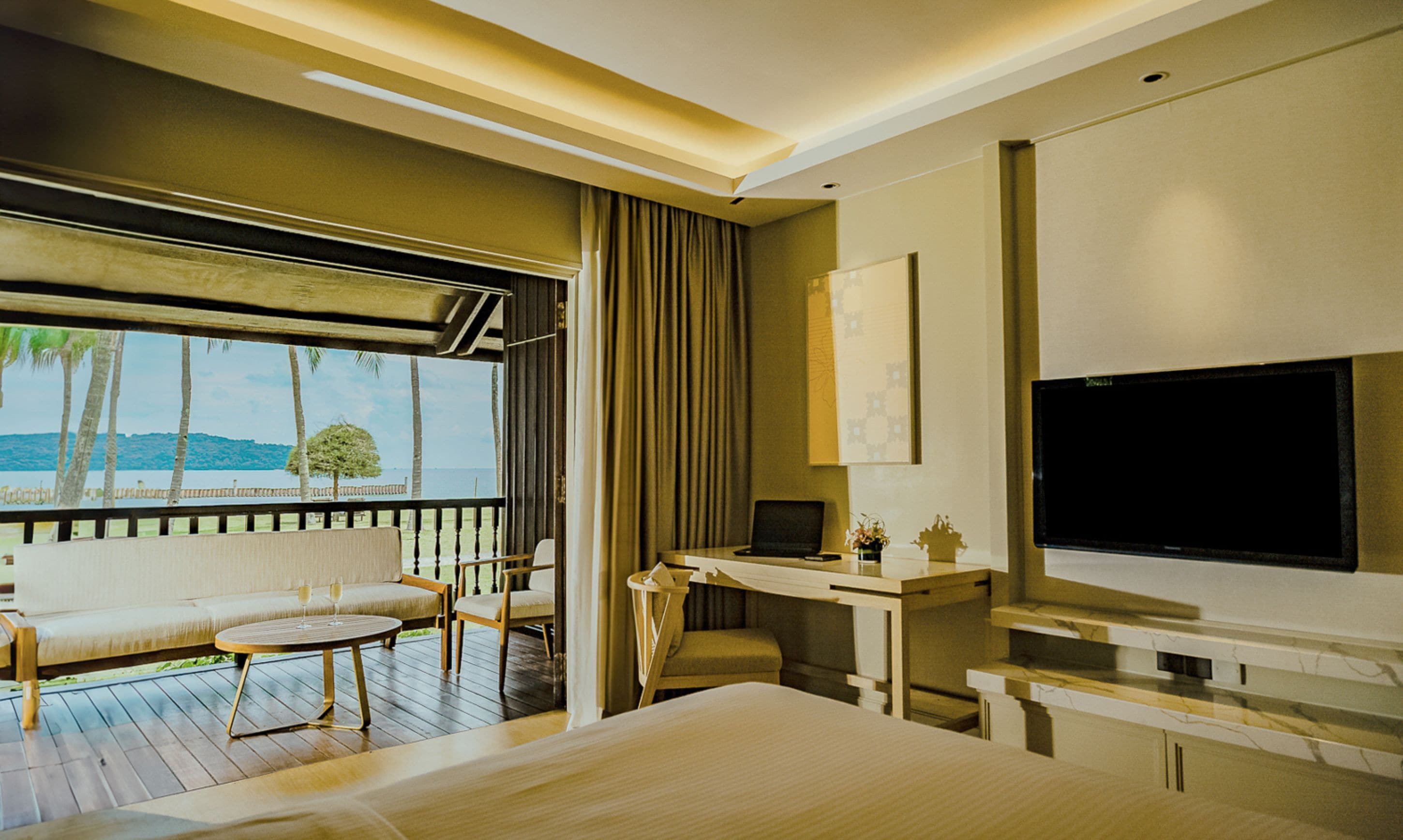 A modern hotel room with a balcony, a sofa, a desk, and a TV.