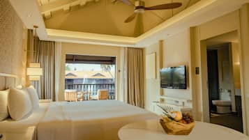 A hotel room with a large bed, a ceiling fan, a TV, and a balcony with a view of buildings.