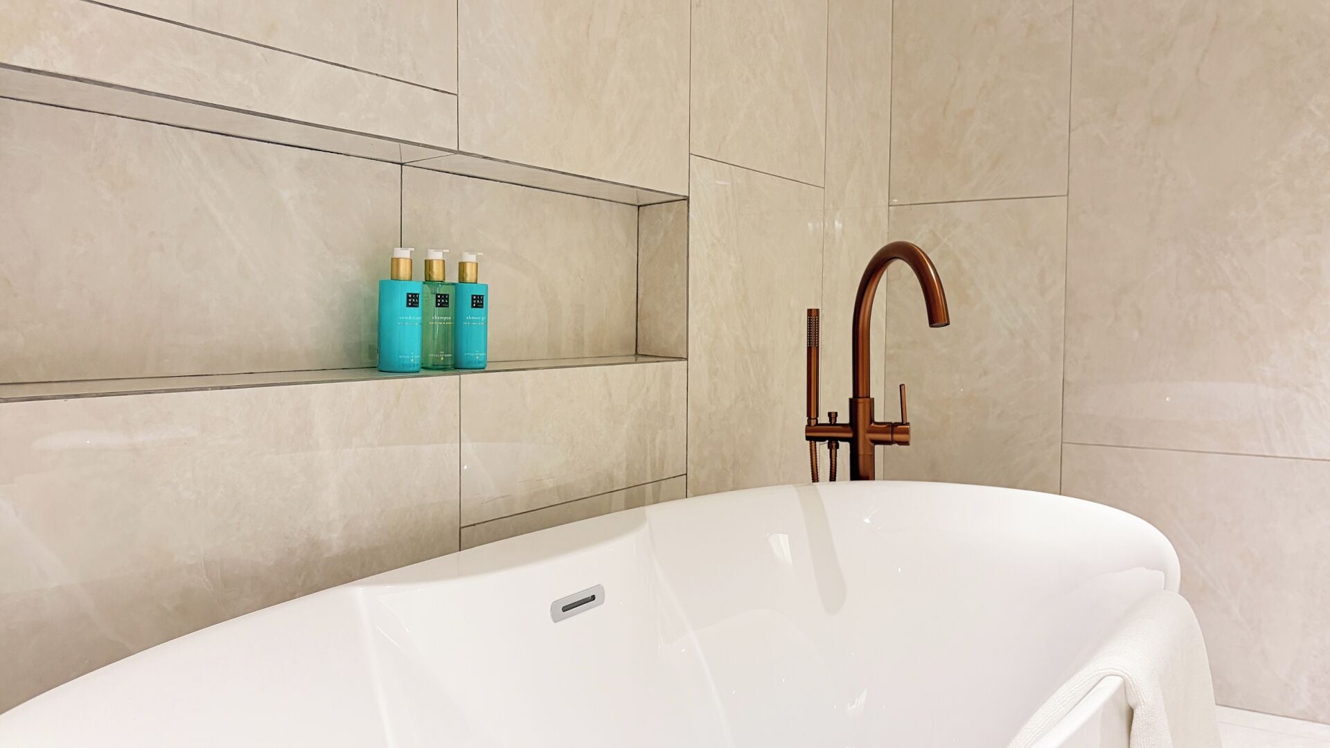 Une salle de bain moderne avec une baignoire sur pieds, une étagère murale pour les articles de toilette et un robinet classique.
