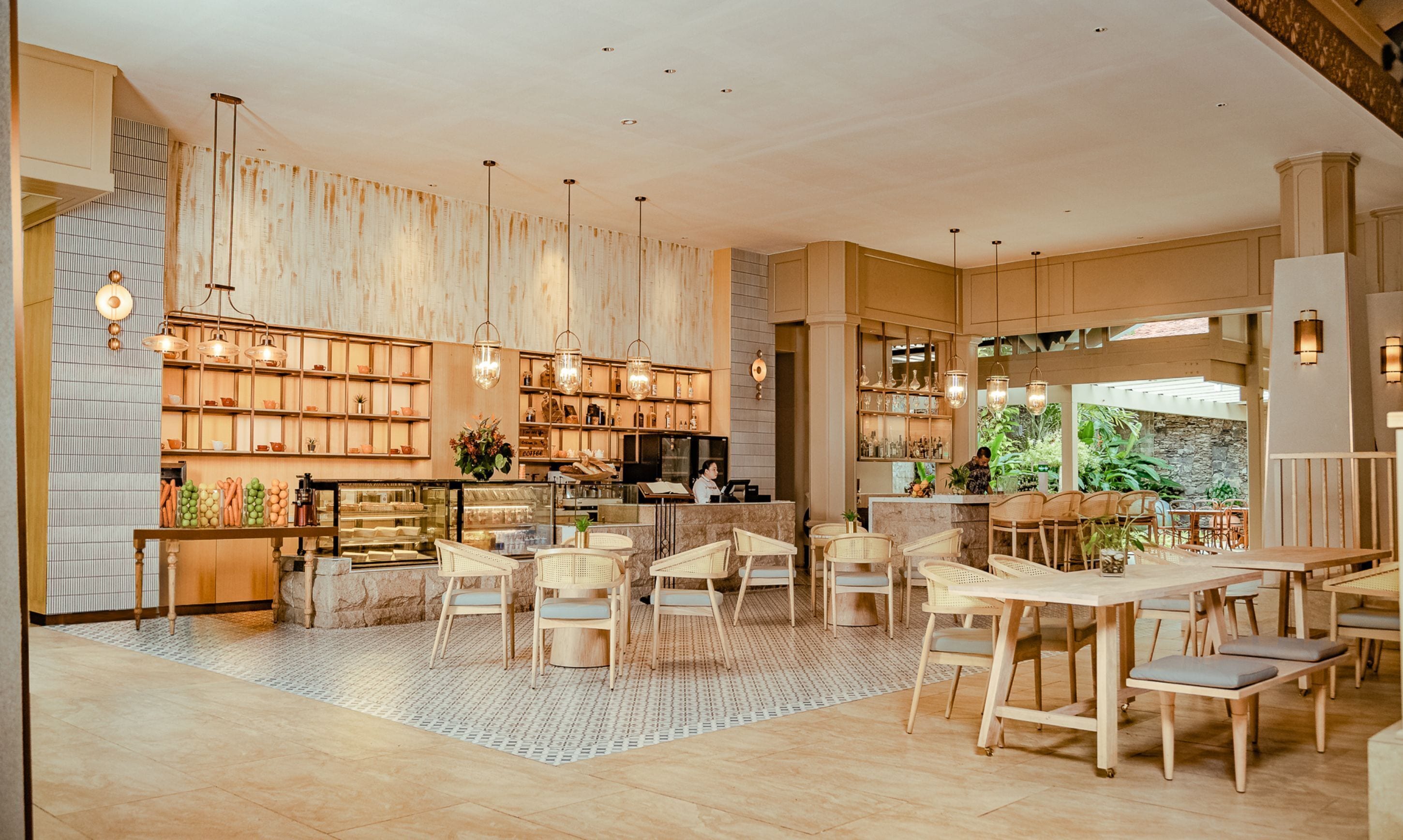 A spacious cafe with wooden furniture, a counter with a barista, and shelves with various items.