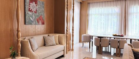A living room with a sofa, a dining table with chairs, a coffee table, and a large window with curtains.