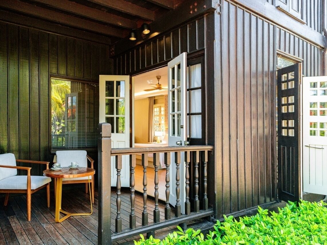 A wooden porch with a table and chairs, a door, and a small garden area.