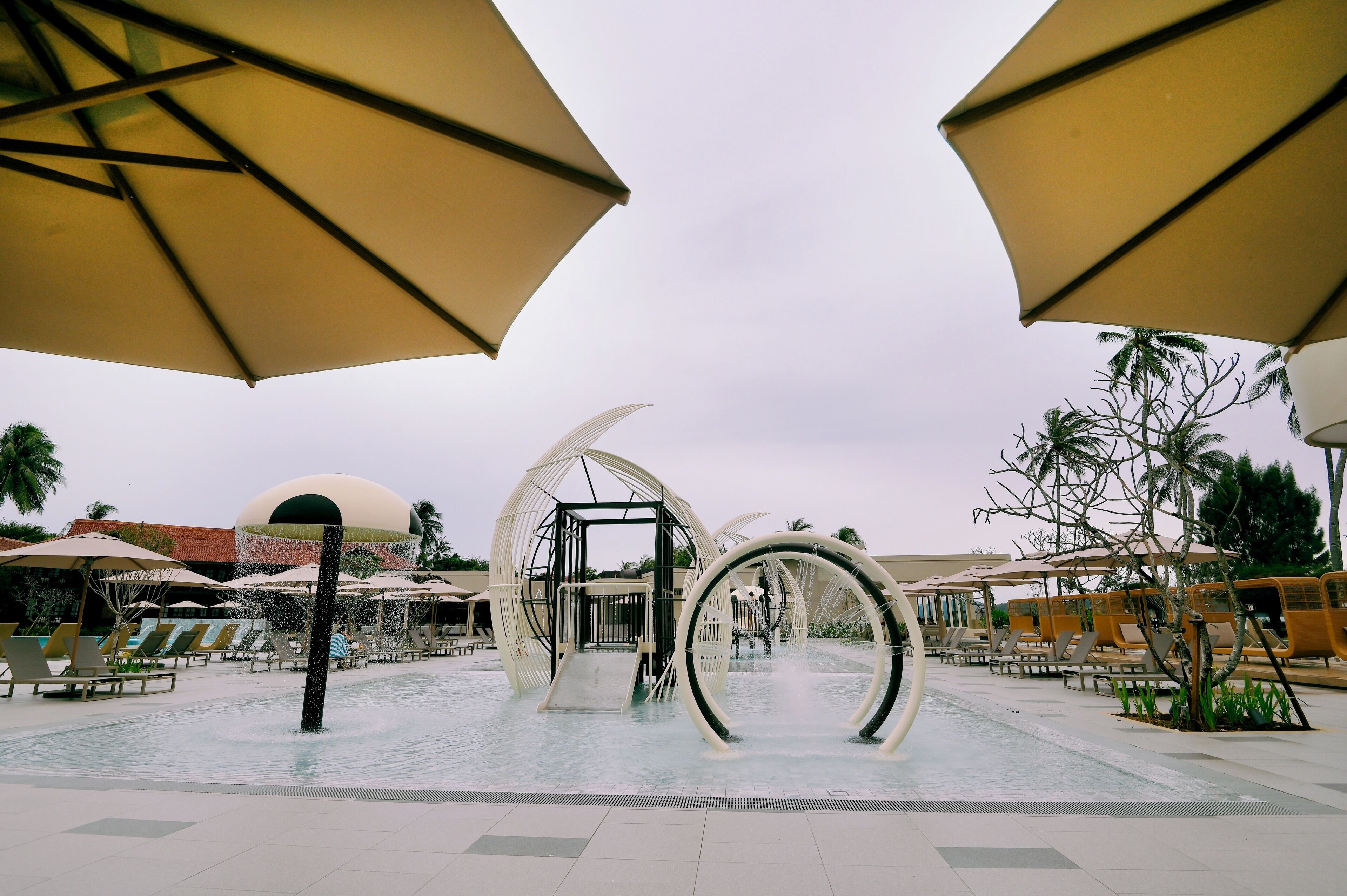 Zona de piscina con sillones de descanso, sombrillas y arcos decorativos.