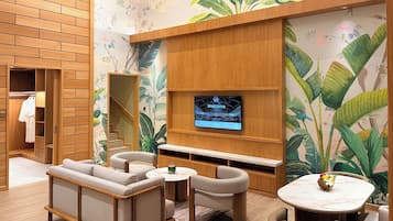Habitación de hotel con pared de madera, televisor, zona de estar y baño con puerta de madera.