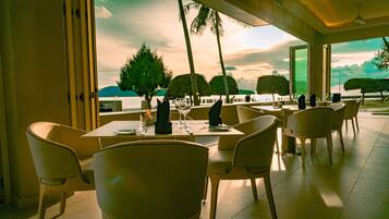 A restaurant with tables and chairs arranged for dining, overlooking a scenic view of trees and a body of water.