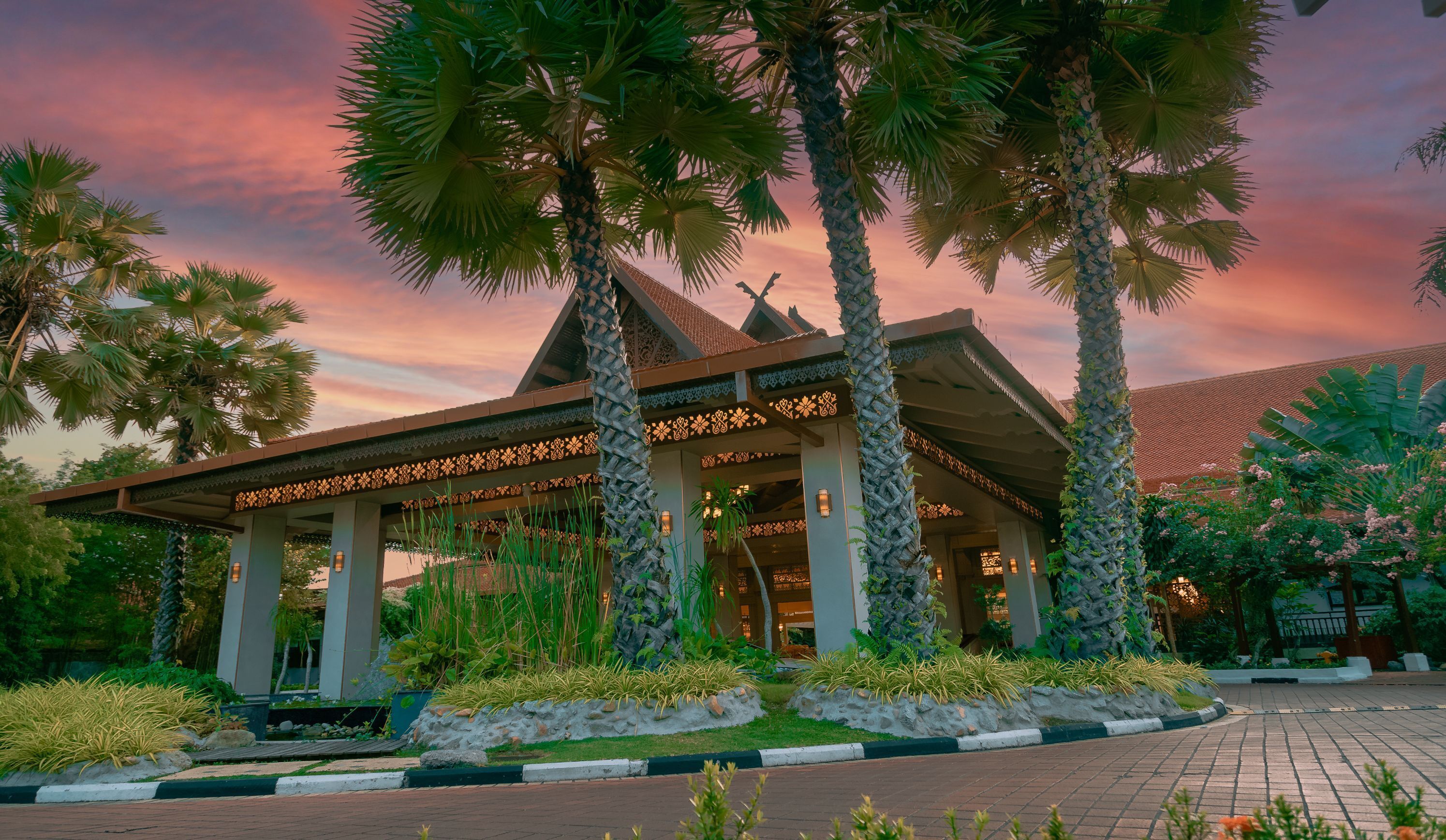 A traditional building with a covered entrance, surrounded by palm trees and well-maintained gardens.