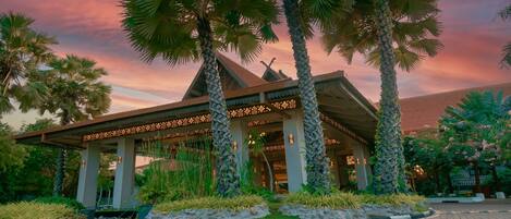 A traditional building with a covered entrance, surrounded by palm trees and well-maintained gardens.