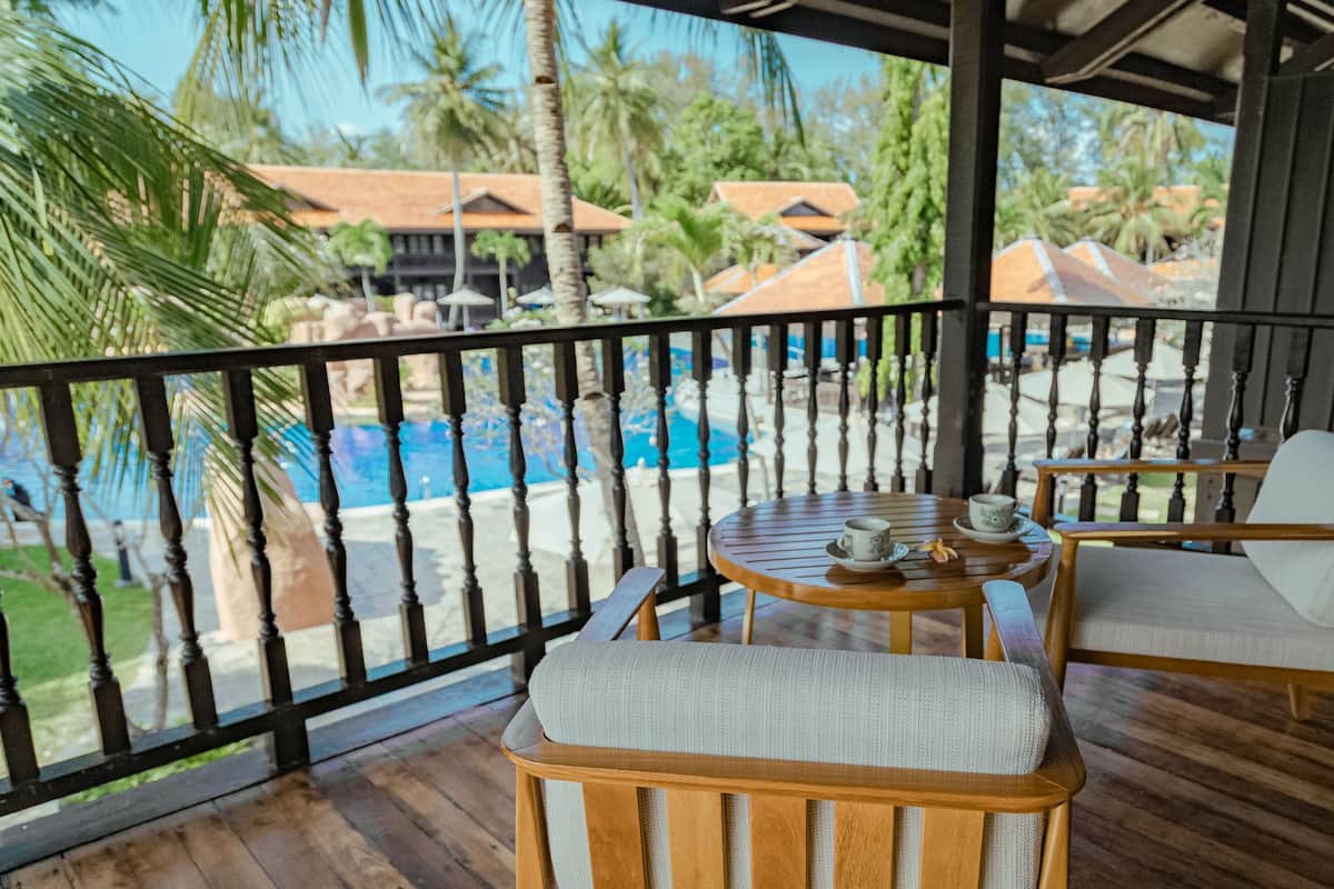Um deck de madeira com vista para a piscina, duas cadeiras e uma mesa com xícara e pires.