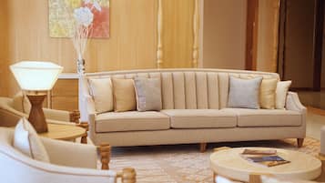 A beige sofa with two pillows, a round wooden coffee table, a floor lamp, and a patterned rug in a well-lit room with wooden paneling.