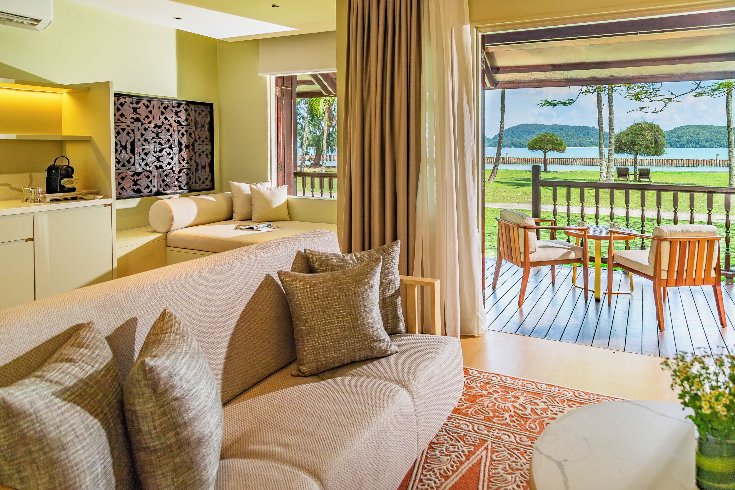 Una habitación de hotel moderna con sofá, una mesa de comedor y vistas a un lago y montañas.