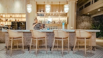 A bar area with a marble countertop, four wicker bar stools, and a bartender.