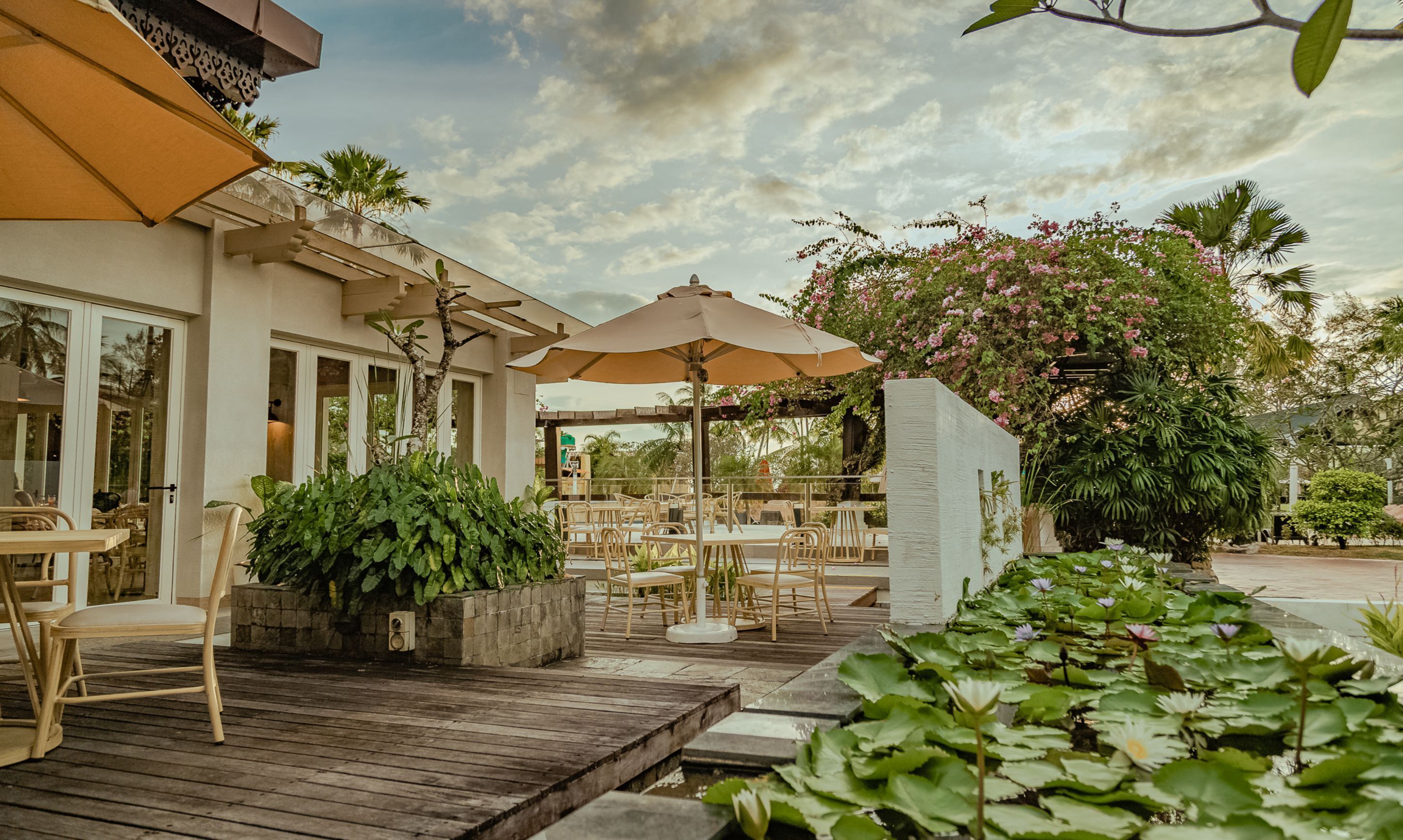 An outdoor patio area with wooden flooring, tables, chairs, and umbrellas.