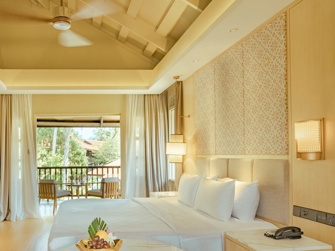 A hotel room with a large bed, a bedside table with a phone, a ceiling fan, and a view of the outdoors.