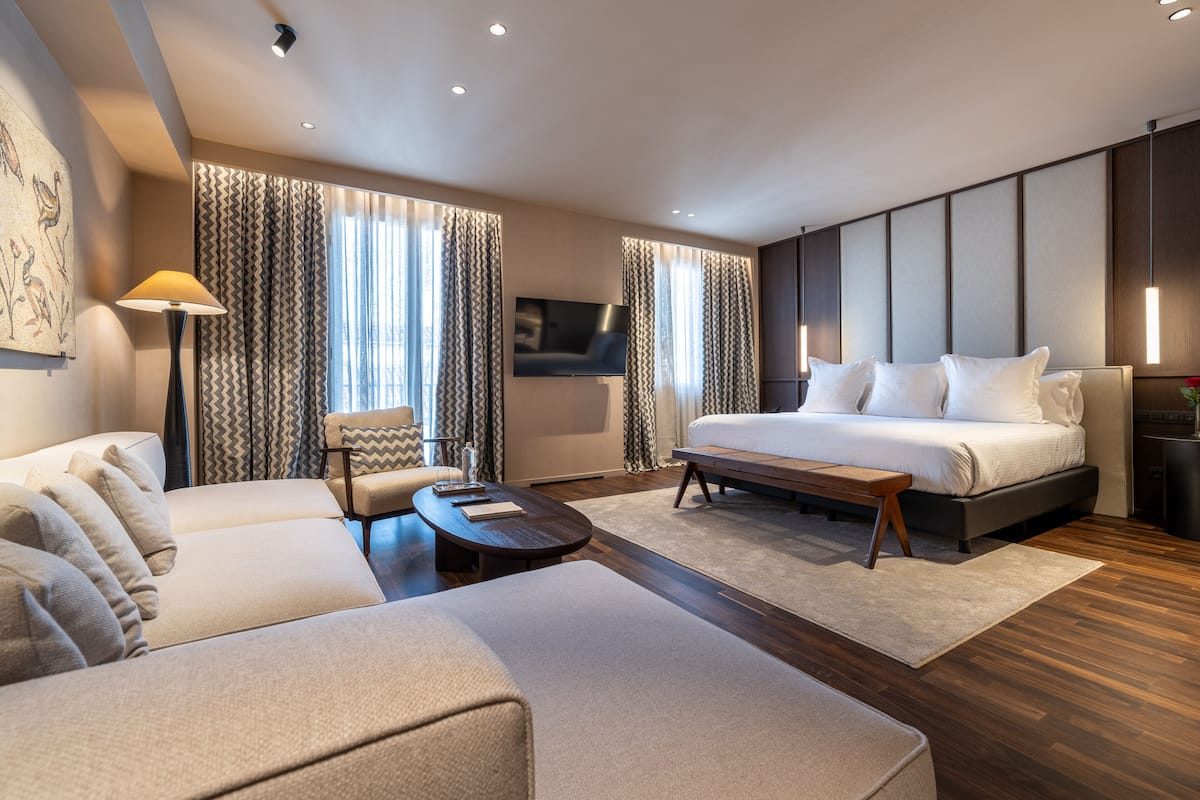 A modern hotel room with a large bed, a sofa, a coffee table, and a TV mounted on the wall.