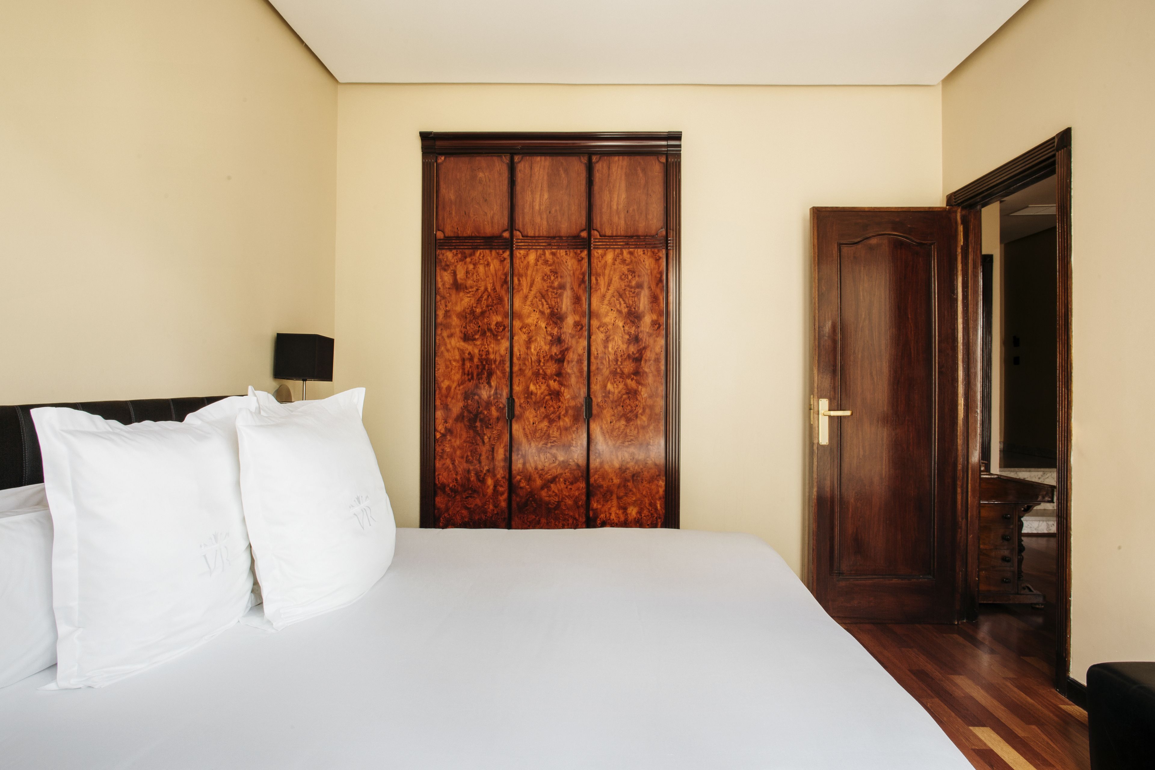 Un dormitori amb un llit gran, un armari de fusta i una porta que dona a una altra habitació.