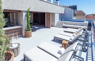 A rooftop bar with outdoor seating, a pool, and a staircase leading to an upper level.