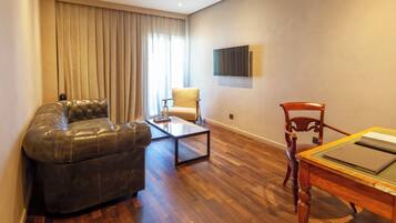 Een woonkamer met een leren bank, een glazen salontafel, een houten eettafel met stoelen en een aan de muur bevestigde televisie.
