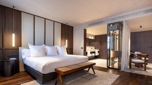 A modern hotel room with a large bed, bedside table, and a bench. There is a bathroom with a mirror and a shower area. - Hotel Villa Real, a member of Preferred Hotels & Resorts (Madrid)