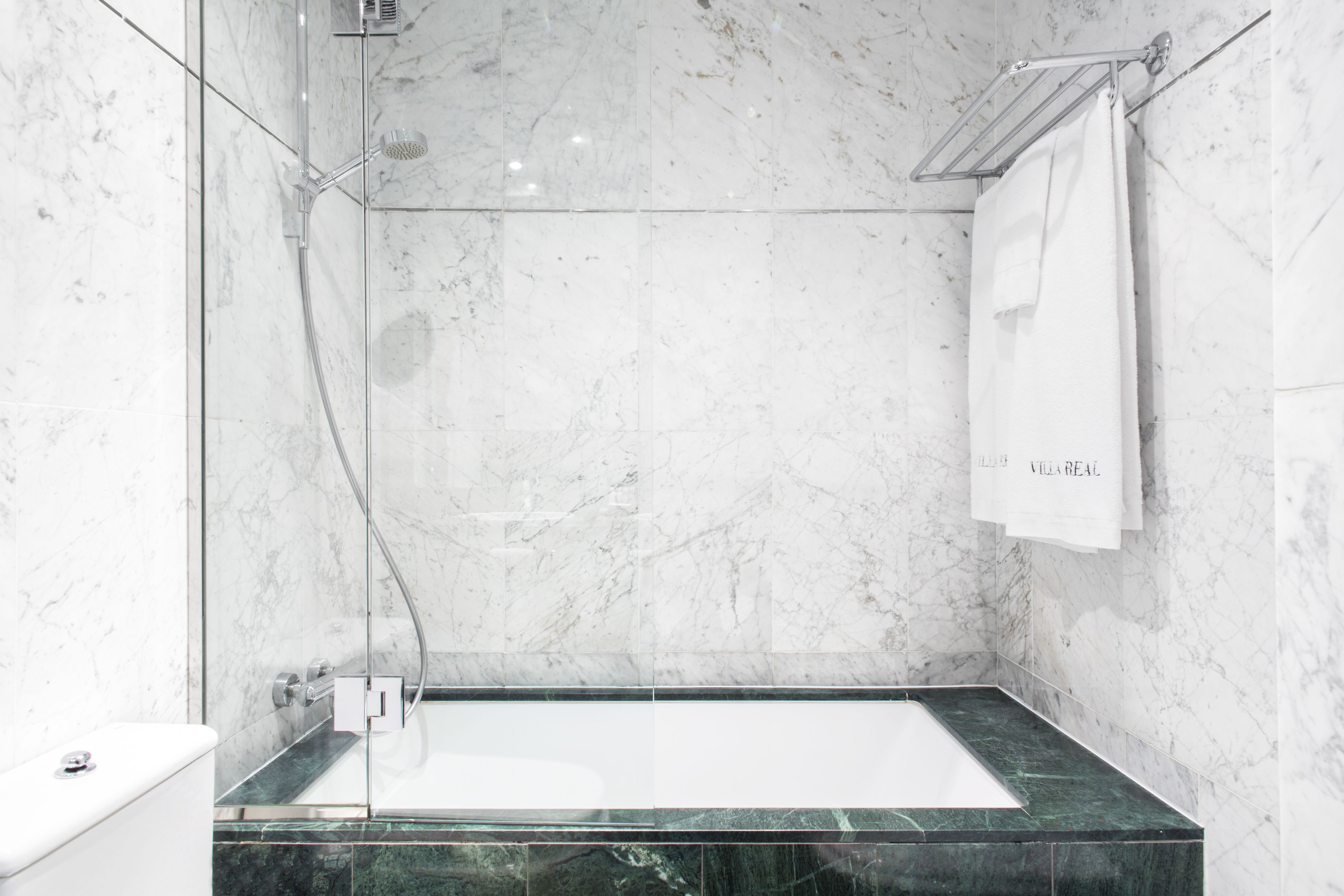 Un baño moderno con ducha envuelta en vidrio, pared de mármol y encimera de mármol verde.