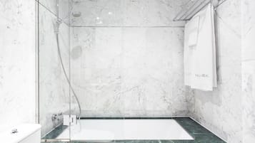 Un baño moderno con ducha envuelta en vidrio, pared de mármol y encimera de mármol verde.