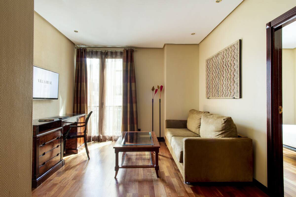 A living room with a sofa, a glass-top coffee table, a TV, and a desk with drawers.