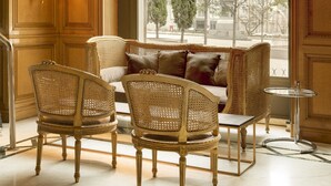 A luxurious room with a large window, ornate wooden paneling, a sofa with cushions, and wicker chairs. - Hotel Villa Real, a member of Preferred Hotels & Resorts (Madrid)
