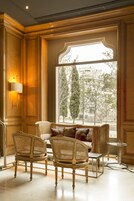 A luxurious room with a large window, ornate wooden paneling, a sofa with cushions, and wicker chairs.