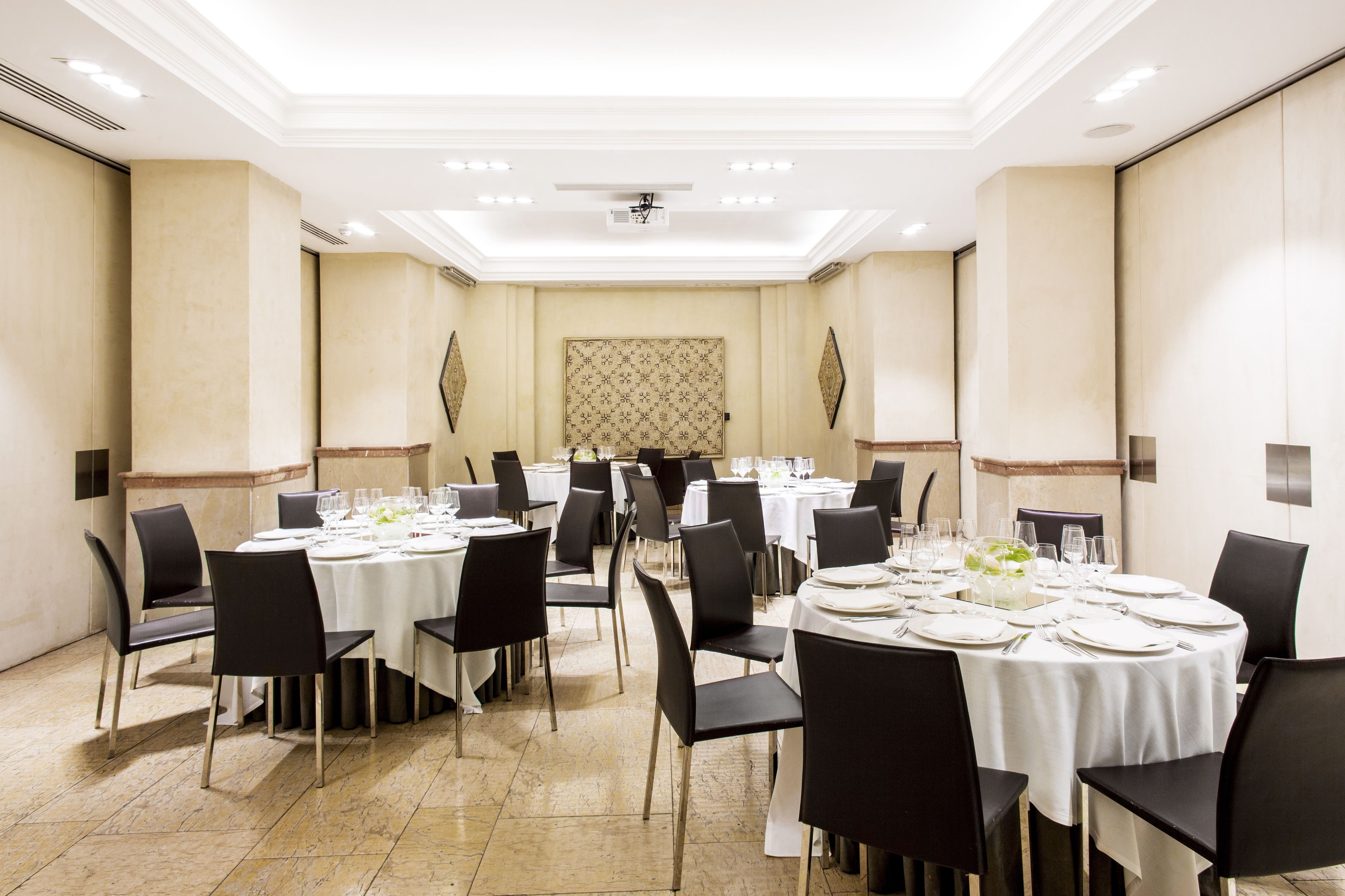 A conference room with multiple round tables set for dining, black chairs, and a patterned wallpaper backdrop.