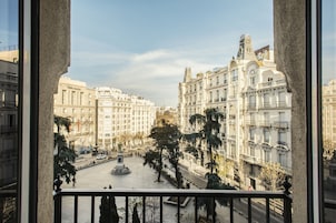 A view from a balcony overlooking a plaza with classical architecture, a central monument, and surrounding buildings.