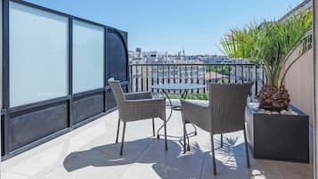 A balcony with two wicker chairs and a small round table, overlooking a cityscape.