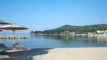 A beach with lounge chairs and umbrellas, a calm sea, and a hilly landscape in the background.