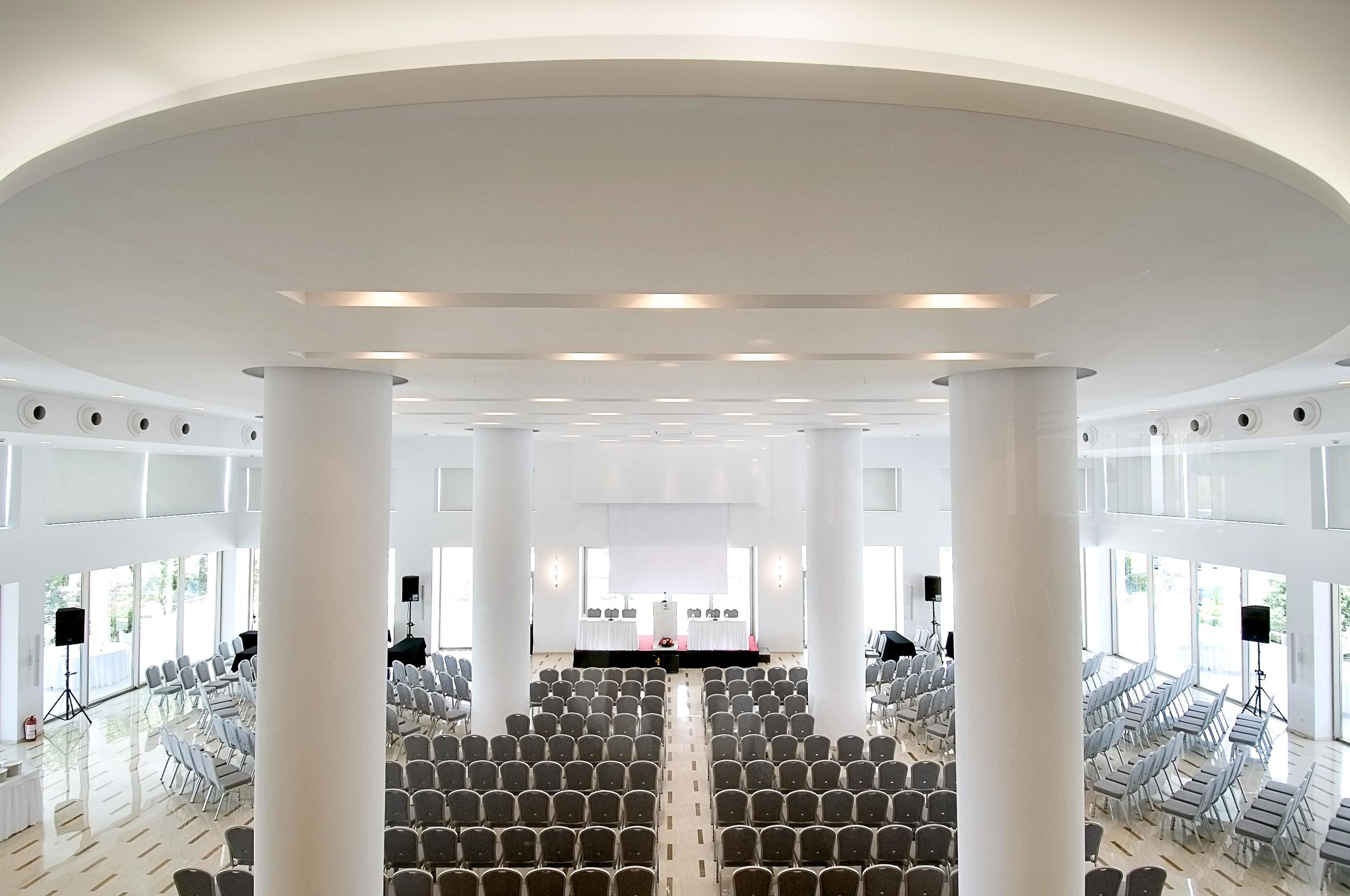 A large, well-lit hall with rows of chairs facing a stage, large windows, and a modern architectural design.