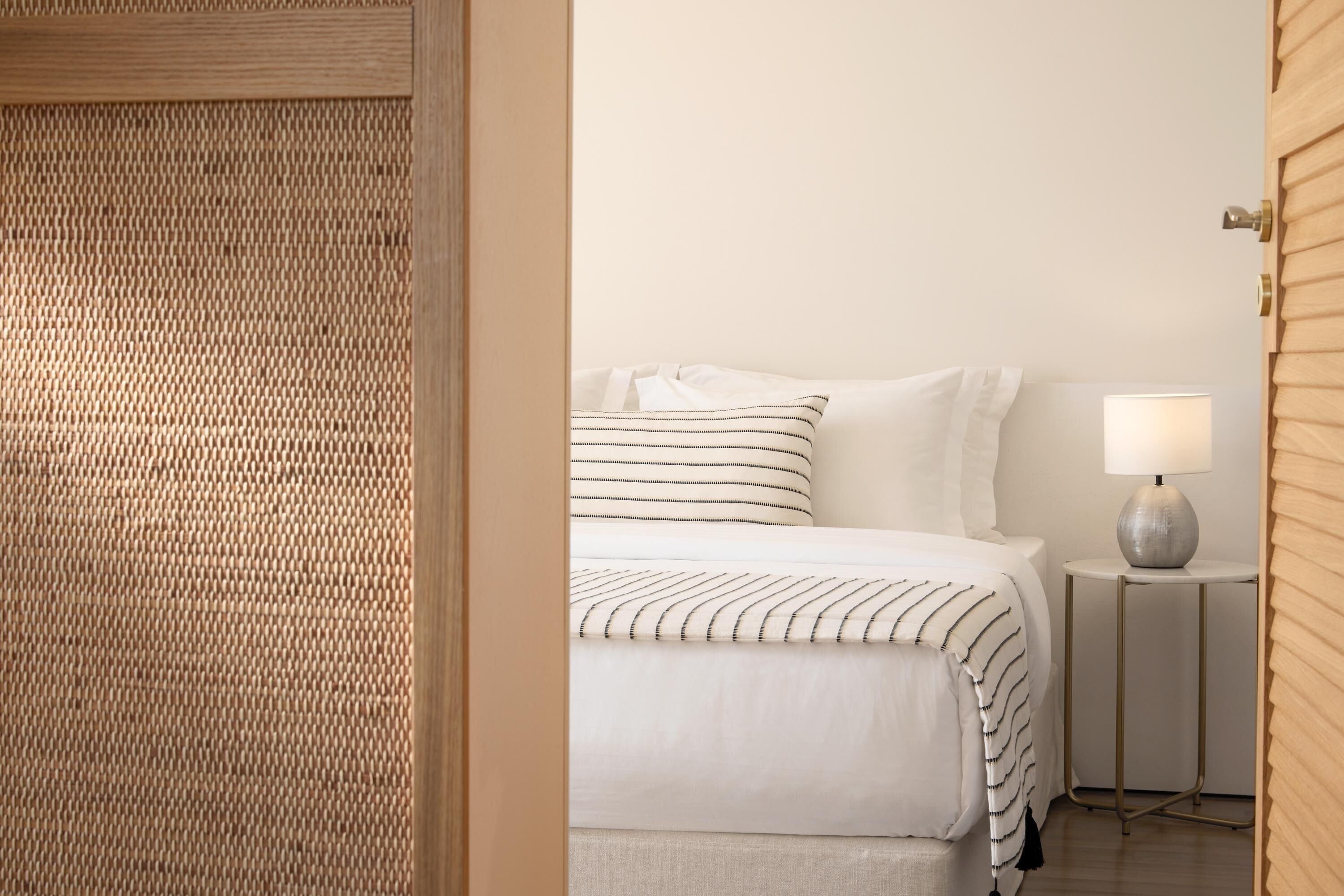 A neatly made bed with striped bedding, a bedside lamp, and a small round table.
