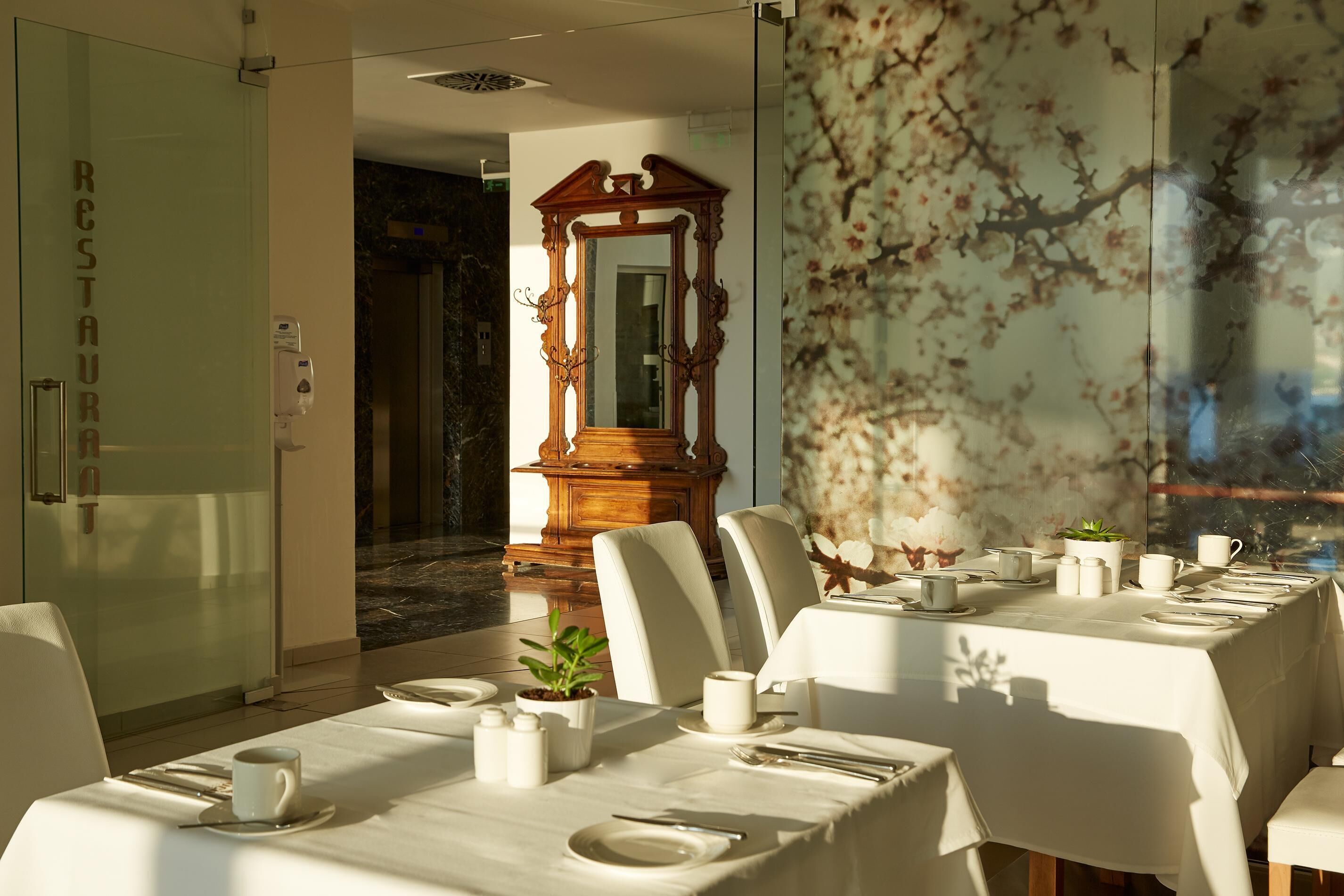 A dining area with tables set for service, a mirror, and a wall with a floral pattern.